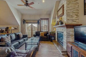 A living room with a fireplace, leather sofas, a coffee table, and a TV. - Main Street condo with balcony, outdoor pool, hot tubs & gym - walk to lifts (Breckenridge)