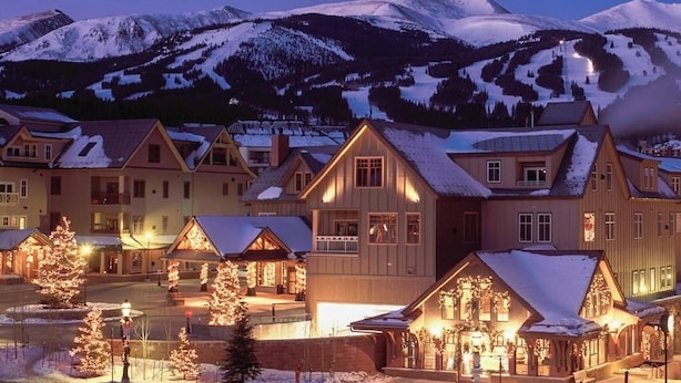 Une ville de montagne enneigée au crépuscule, avec des bâtiments illuminés et une station de ski en arrière-plan.