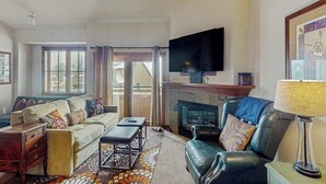 Un salon comprenant un canapé, un fauteuil, une cheminée, un téléviseur et un tapis à motifs.