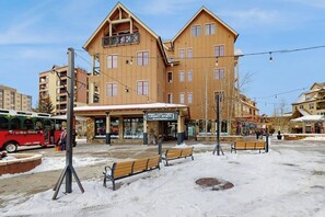 Un immeuble à plusieurs étages, avec un magasin d’articles de sport au rez-de-chaussée, des bancs dans la neige et un autobus en arrière-plan.