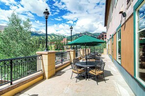 Un patio al aire libre con mesas y sillas, un paraguas verde y vistas a las montañas.