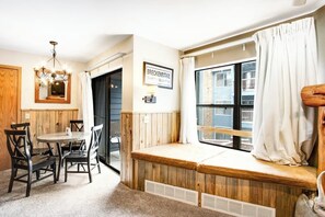 Ein gemütliches Zimmer mit einer hölzernen Sitzbank, einem Esstisch mit Stühlen, einer Kandelaber und einem Fenster mit Vorhängen.