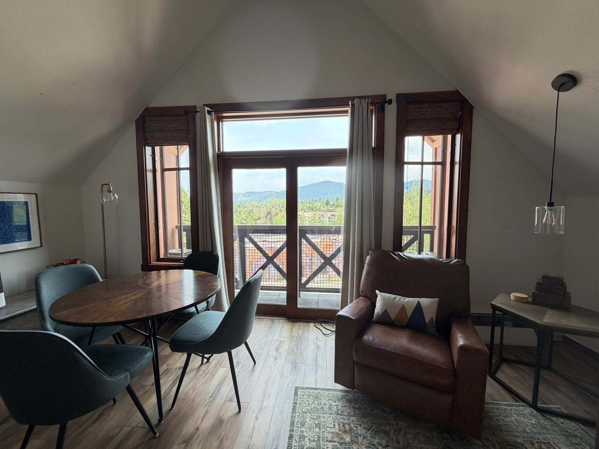A room with a dining table, chairs, a sofa, a small side table, and a hanging light fixture.