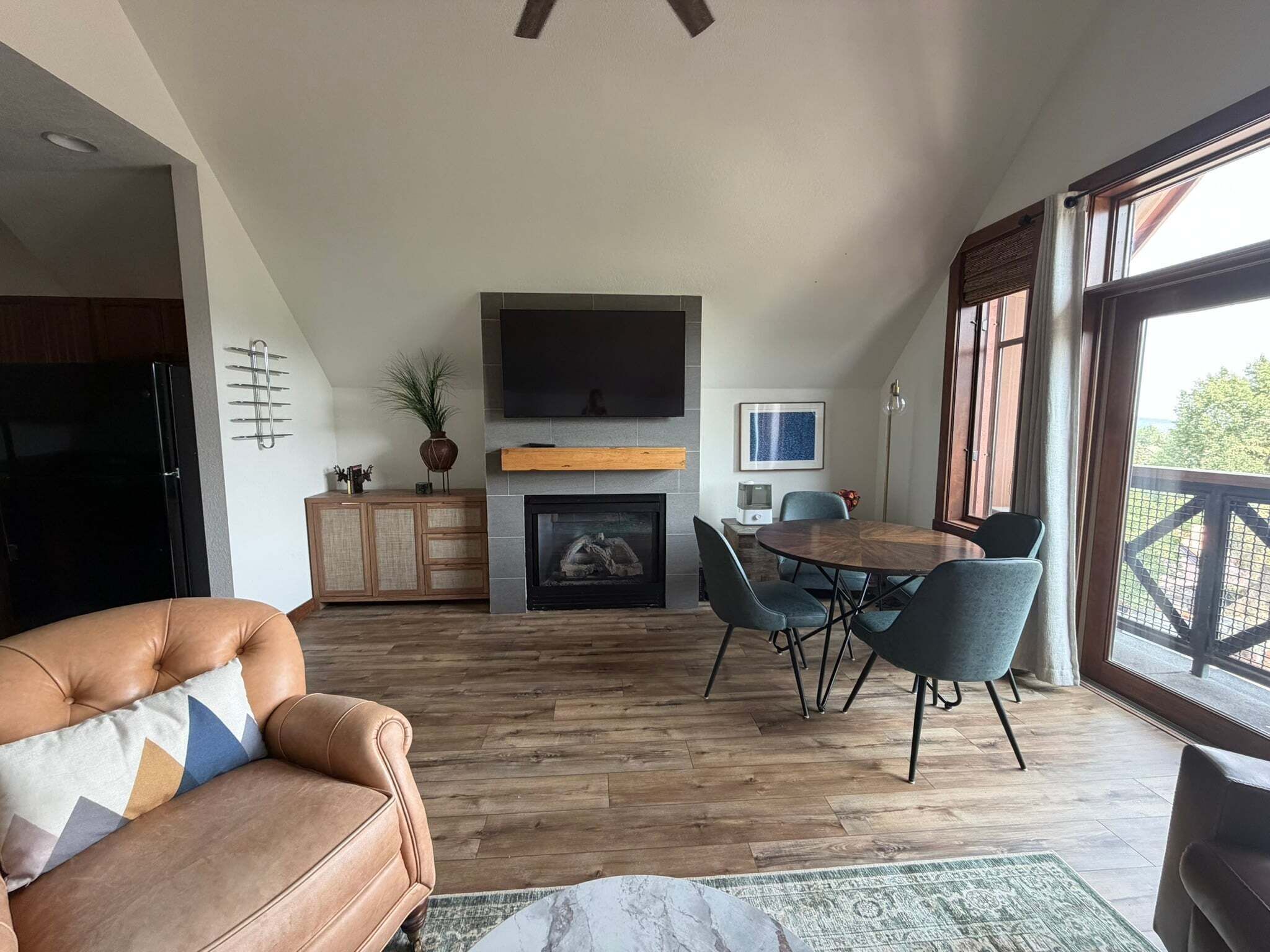 A spacious living area with a fireplace, a dining table with chairs, a leather sofa, and a large window with a view.