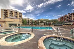 Ein Hotel mit einem großen Außenpool, mehreren Whirlpools und einer Bergkulisse.