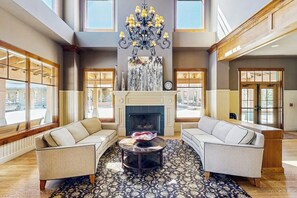 Eine großzügige Lobby mit Kamin, zwei Sofas, einem Kronleuchter und großen Fenstern.