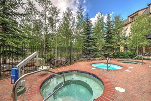 Ein Poolbereich mit zwei Whirlpools, umgeben von einer Ziegelterrasse und einem Metallzaun.