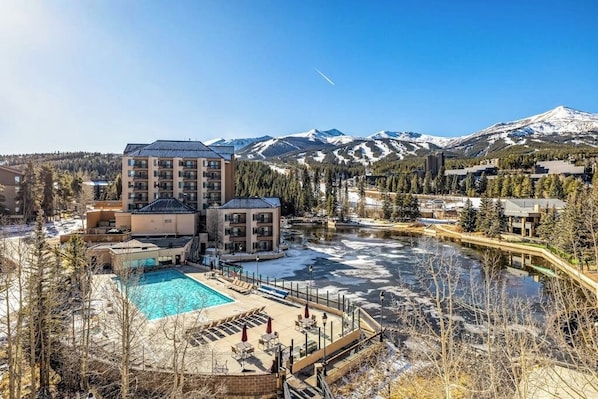 Ein Hotel mit Pool, umgeben von schneebedeckten Bergen und Bäumen.