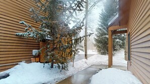Un sendero cubierto de nieve que conduce a un edificio con revestimiento de madera y un porche cubierto.