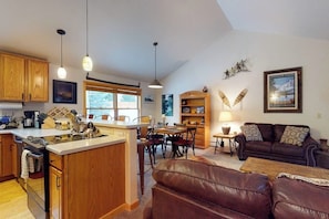 A kitchen with wooden cabinets, a dining area with chairs, a sofa, and a lamp. - Modern Keystone condo w/ a gas fireplace & shared hot tub (Keystone)