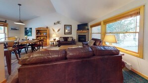 Una sala de estar con un sofá de cuero marrón, una chimenea, un televisor y un comedor con sillas y una mesa.