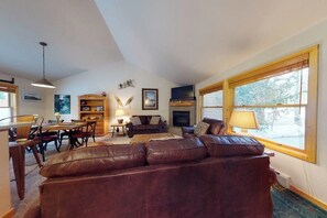 A living room with a brown leather sofa, a fireplace, a television, and a dining area with chairs and a table. - Modern Keystone condo w/ a gas fireplace & shared hot tub (Keystone)