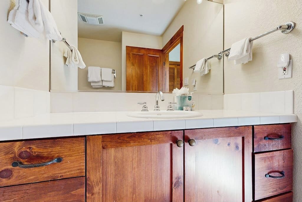 A bathroom with a wooden vanity, a large mirror, a sink, and towel racks.