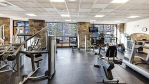 Een sportschool met fitnessapparatuur, grote ramen en een stenen zuil.