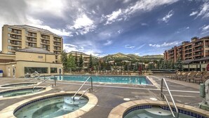 Een hotel met een groot buitenzwembad, diverse jacuzzi's en een bergachtige achtergrond.