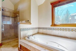 Ein Badezimmer mit einer großen Badewanne, einer Dusche und einem Fenster mit Blick auf Bäume.