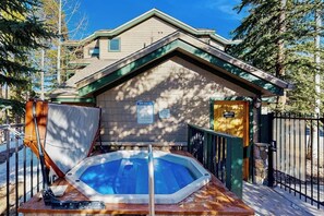A spa with a hot tub, a wooden deck, and a building with a green roof. - Delightful condo with hot tub, gas fireplace & heated garage (Breckenridge)