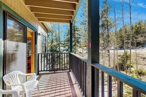 A wooden deck with a railing, a white plastic chair, and a view of trees and a building in the background. - Delightful condo with hot tub, gas fireplace & heated garage (Breckenridge)