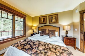 Quarto com uma cama grande, duas mesinhas de cabeceira, uma janela com vista e duas molduras na parede.