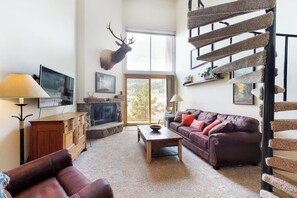 Ein Wohnzimmer mit Kamin, einem aufgehängten Elchgeweih, einer Treppe und einem Fernseher.