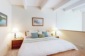 Ein Schlafzimmer mit einem großen Bett, zwei Nachttischen mit Lampen, einem gerahmten Bild an der Wand und einem Fenster.