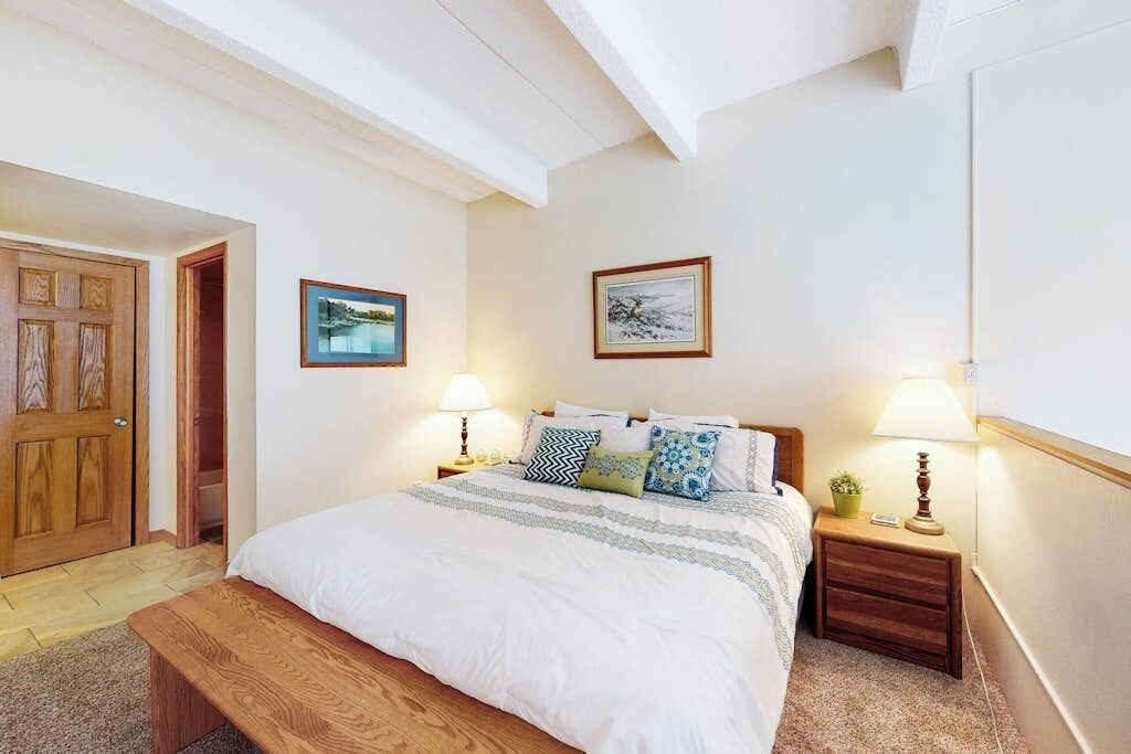 A bedroom with a bed, bedside tables, a bench, and two wall-mounted lamps.