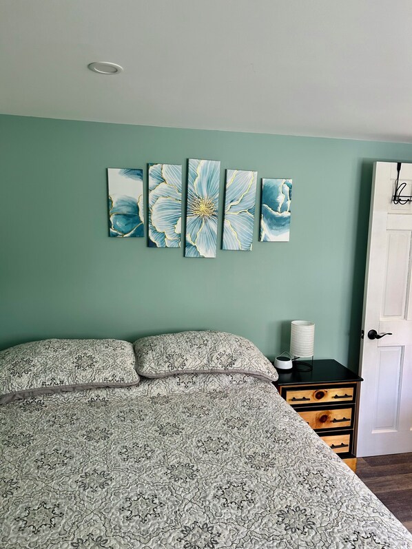 Un lit avec une couvre-lit à motifs, une table de chevet avec une lampe et une porte avec une poignée.