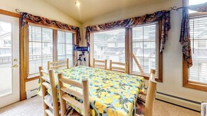 Ein Zimmer mit Holztisch und Stühlen, großen Fenstern mit Jalousien und einem Teleskop auf einem Stativ.