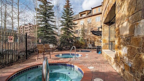A pool area with two hot tubs, a brick pathway, and a stone building. - Charming, walk-to-lifts condo with hot tubs, pool, gym & gas fireplace (Breckenridge)