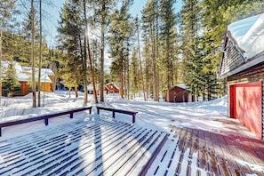 Eine Holzterrasse mit Bänken, umgeben von verschneitem Gelände und hohen Kiefern.