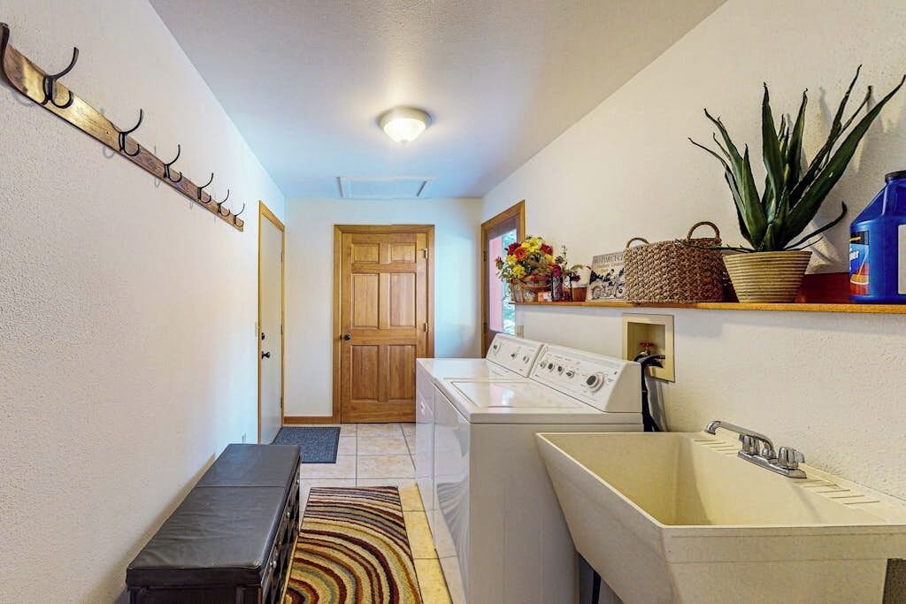 A laundry area with a washing machine, a sink, a bench, and a coat rack.