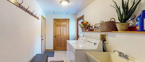 A laundry area with a washing machine, a sink, a bench, and a coat rack.