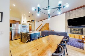 A modern kitchen with a central island, a dining area with a wooden table, and a living space with a fireplace.