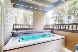 A spa area with a hot tub, wooden deck, and a view of trees.