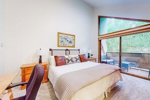 A bedroom with a bed, a desk, a chair, a nightstand, a lamp, a framed picture, and a balcony with outdoor furniture. - King's Crown | Townhouse in Breckenridge with hot tub & fireplace, walk to lifts (Breckenridge)