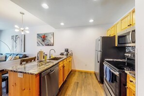 Eine moderne Küche mit Holdekor, einer Arbeitsplatte aus Granit, Edelstahlgeräten und einem Essbereich mit Sofa und Tisch.