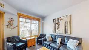Ein modernes Wohnzimmer mit einer Couch, zwei Sesseln, einem Couchtisch und einem großen Fenster.