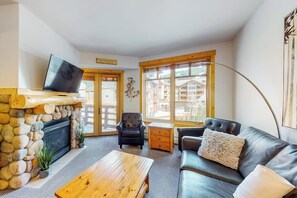 Ein Wohnzimmer mit Kamin aus Stein, einem Fernseher, einer Couch und einem Couchtisch.