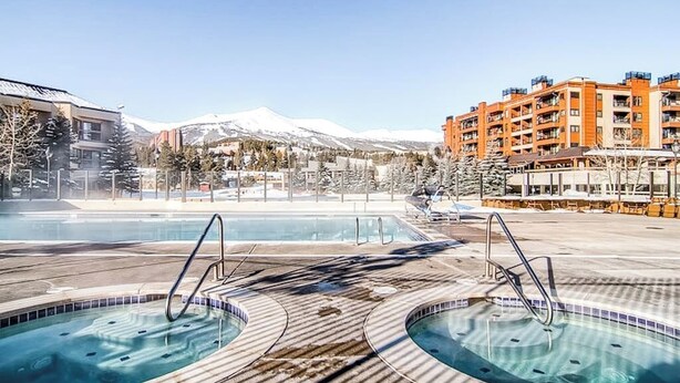 Ein Poolbereich mit Whirlpools, Blick auf die Berge und ein Gebäude mit Balkonen.
