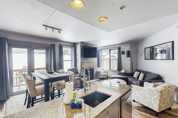 A modern kitchen with granite countertops, a built-in stove, and a dining area with a table and chairs. - Ski-in/out condo in Center Village with hot tub, sauna, gym & fireplace (Copper Mountain)