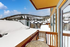 A snow-covered landscape with a wooden balcony overlooking a ski resort. - Ski-in/out condo in Center Village with hot tub, sauna, gym & fireplace (Copper Mountain)