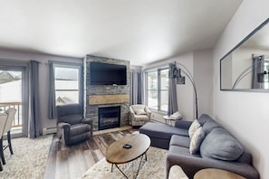 A living room with a fireplace, a sofa, a chair, and a coffee table. - Ski-in/out condo in Center Village with hot tub, sauna, gym & fireplace (Copper Mountain)