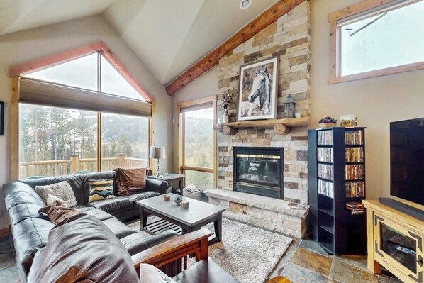 Ein gemütliches Wohnzimmer mit Kamin aus Stein, einer Ledersofa, einem Couchtisch und einem Bücherregal.