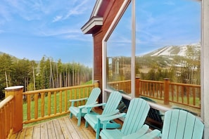 Eine Holzterrasse mit Adirondack-Stühlen und Blick auf ein bewaldetes Gebirge.