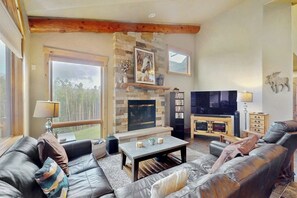 Ein gemütliches Wohnzimmer mit Kamin aus Stein, Ledersofas, einem Fernseher und einem Bücherregal.