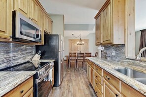 A kitchen with wooden cabinets, a granite countertop, a stainless steel sink, and a dining area with a chandelier. - Family-Friendly Townhouses with WiFi, Wood Fireplaces, and Private Washer/Dryers (Breckenridge)
