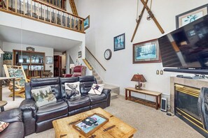 A spacious living room with a leather sofa, a wooden coffee table, a fireplace, and a television. - Cozy condo w/ a private hot tub & Fraser Valley views (Fraser)