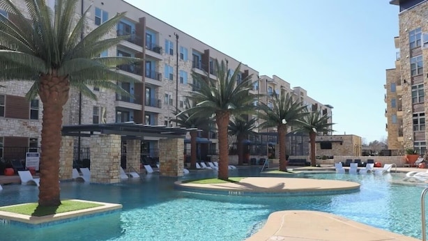 A swimming pool with lounge chairs, palm trees, and multi-story buildings in the background. - King Bed + Queen Bed - In the Heart of Addison’s Social Scene (Addison)