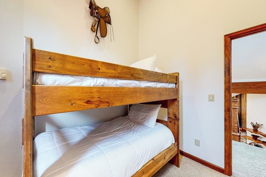 A bunk bed with white bedding, a wooden headboard, and a mirror on the adjacent wall.