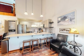 A modern kitchen with a central island, bar stools, a black leather sofa, and a dining table.